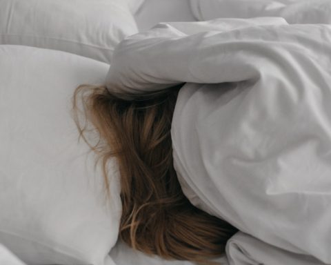 a woman is hiding under a blanket on a bed