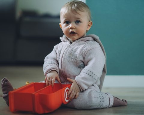 toddler sitting on ground while holding red plastic case